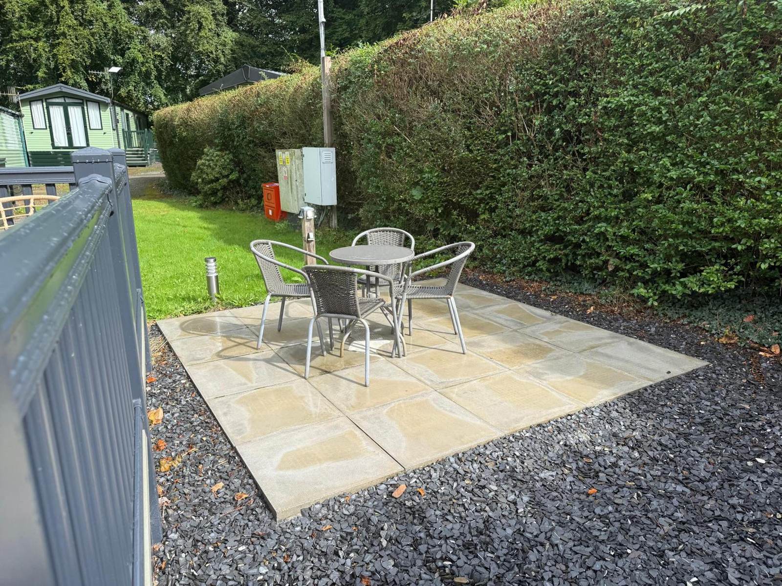 A paved patio with a round bistro table and four chairs against a tall hedge