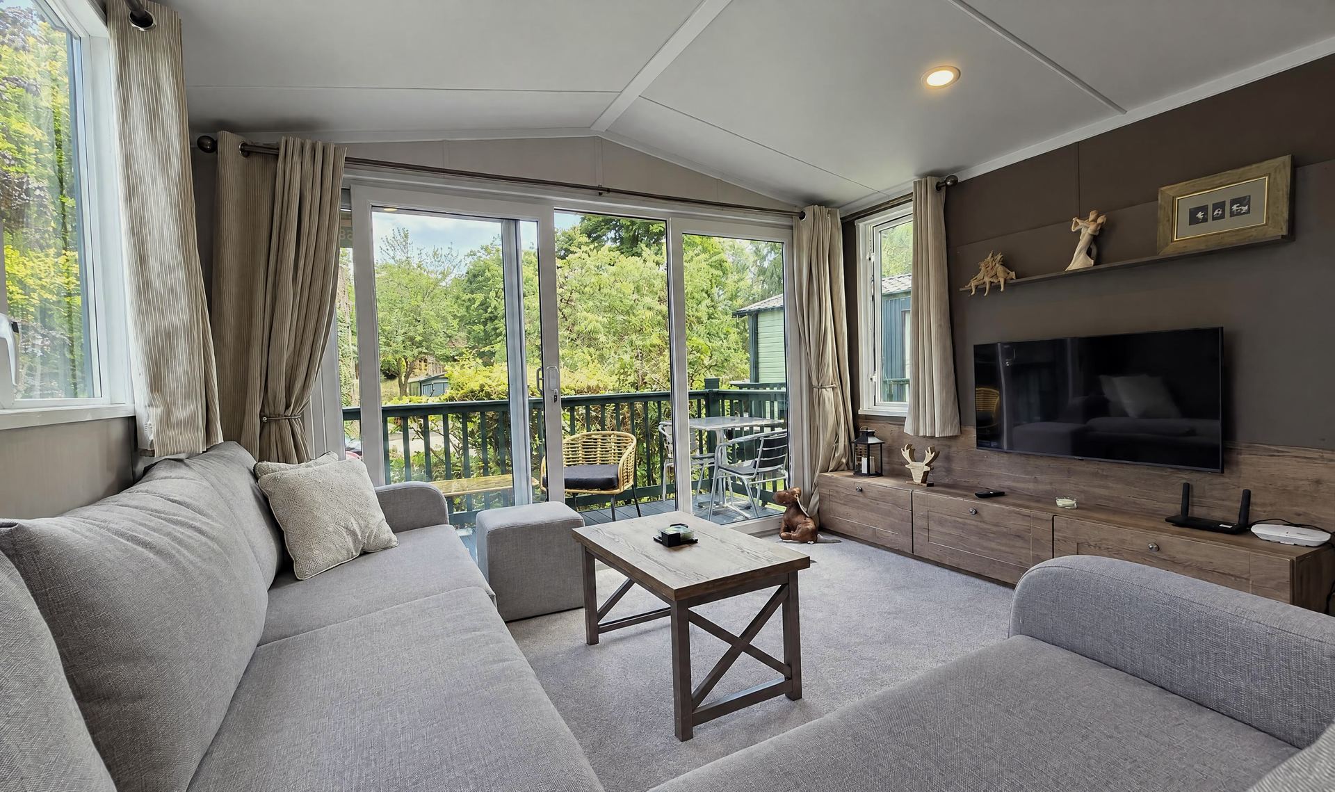 A grey corner sofa and a wall-mounted TV, with glass doors open onto the deck