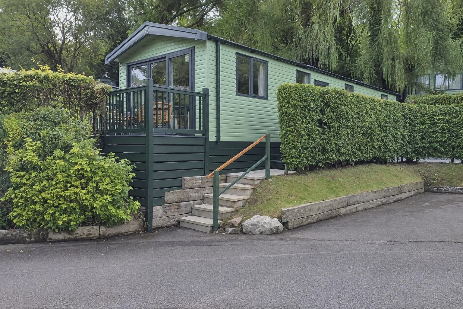 A holiday home with green cladding and a raised deck, seen from the road