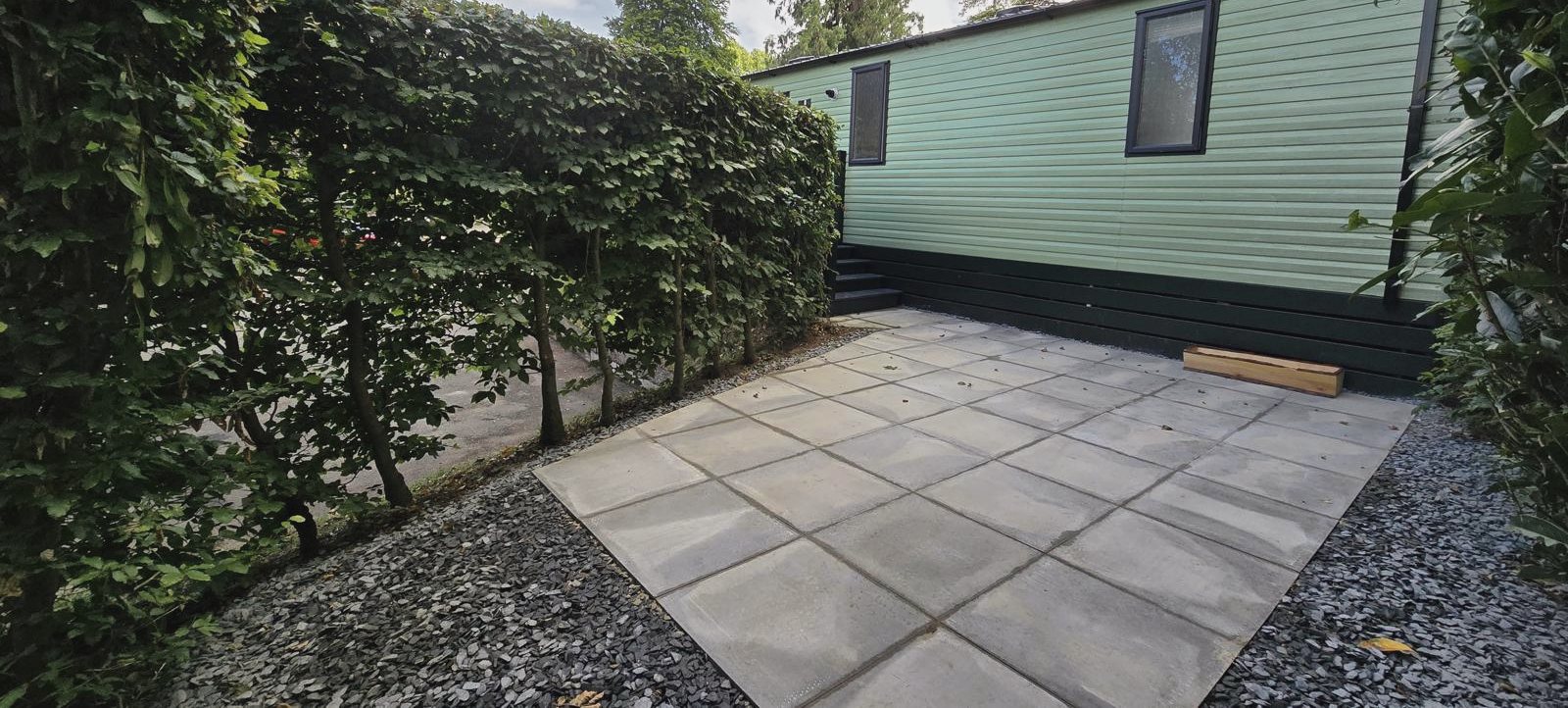 A paved patio with gravel borders, enclosed by a tall hedge