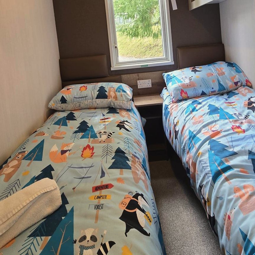 A twin bedroom with two single beds in bright patterned bedding under a window