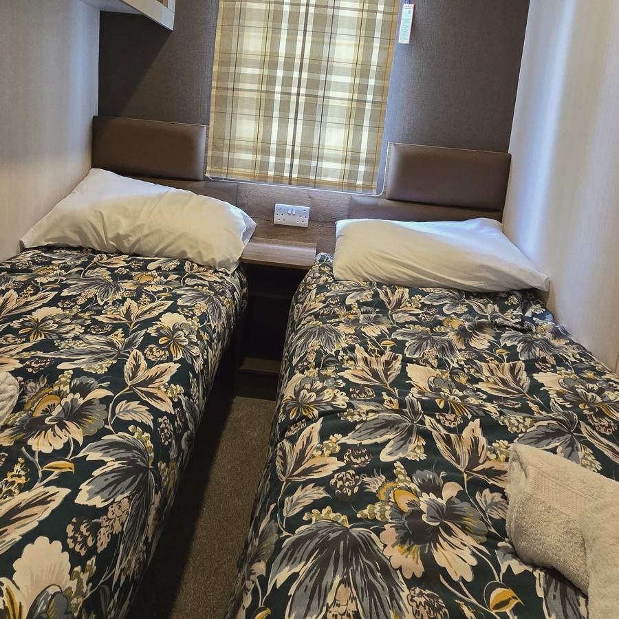 The second twin room: two single beds in dark floral bedding either side of a small shelf, under a window with checked curtains
