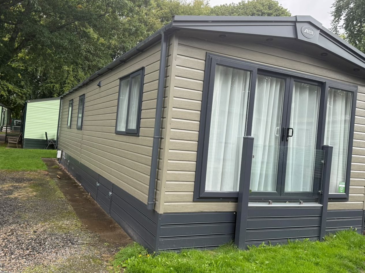 The far end of the holiday home: olive cladding, charcoal trim and tall glazed doors, with grass in front